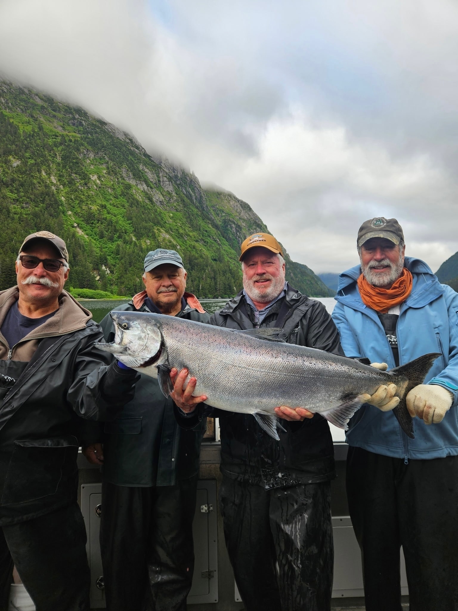 Four anglers holding a large king salmon with dramatic Alaska mountain backdrop