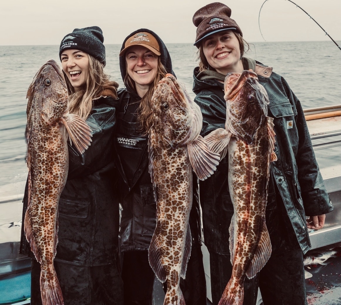 Three women holding large lingcod catches on the boat