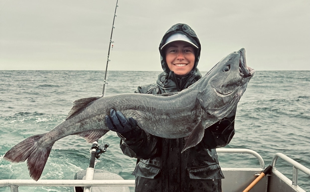 Angler holding a large black cod on a boat in Alaska