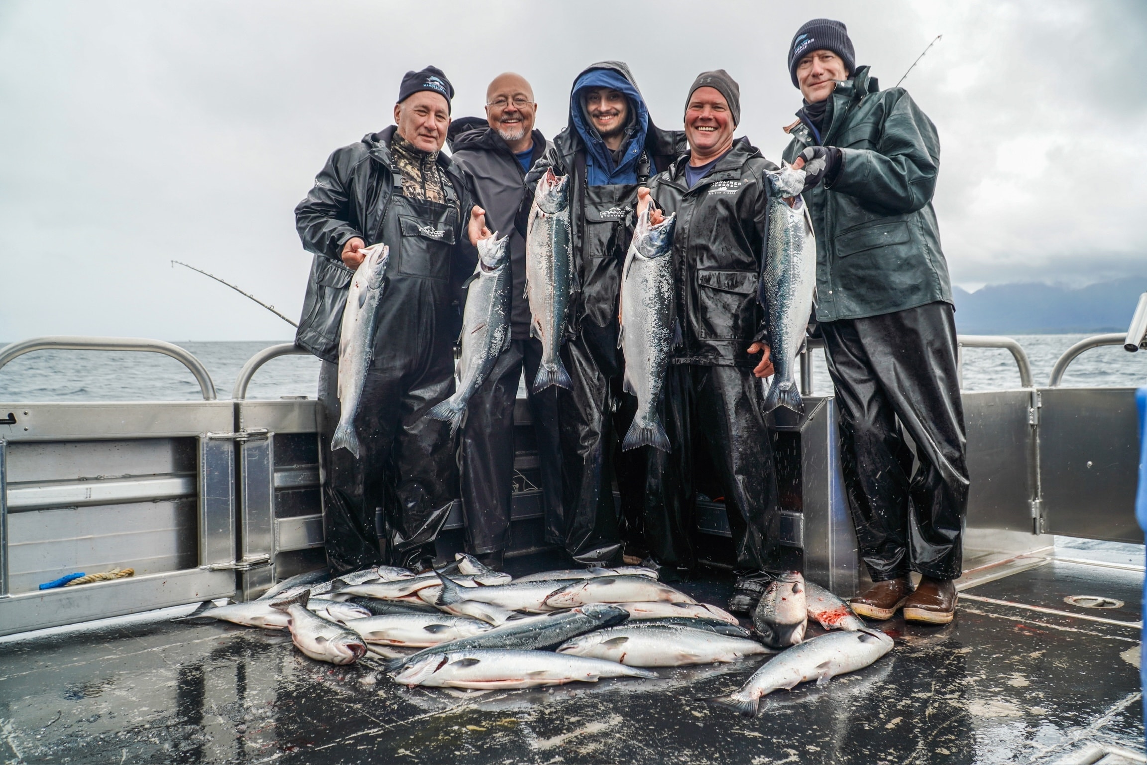 Group of five anglers holding silver salmon on a boat in Alaska